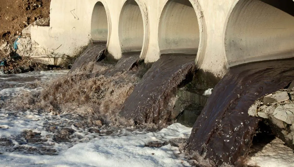 black water flowing out from multiple arch-shaped drains into a river