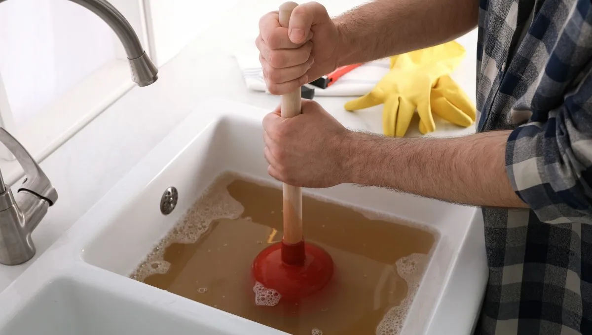 A man clearing a clogged sink, which can cause smelly drains