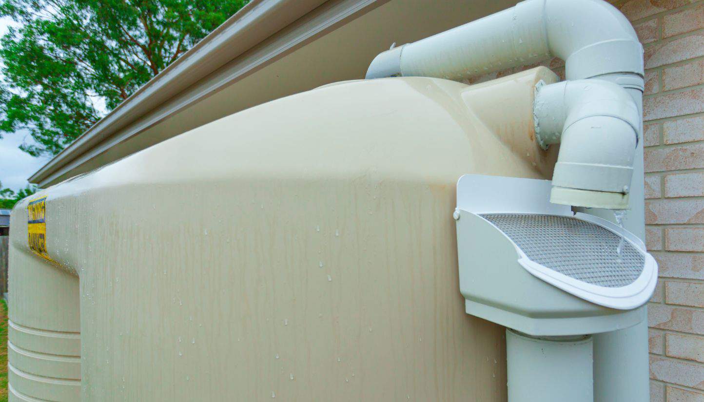 Large rainwater tank collecting rainwater from a house roof, with a filtering system attached.