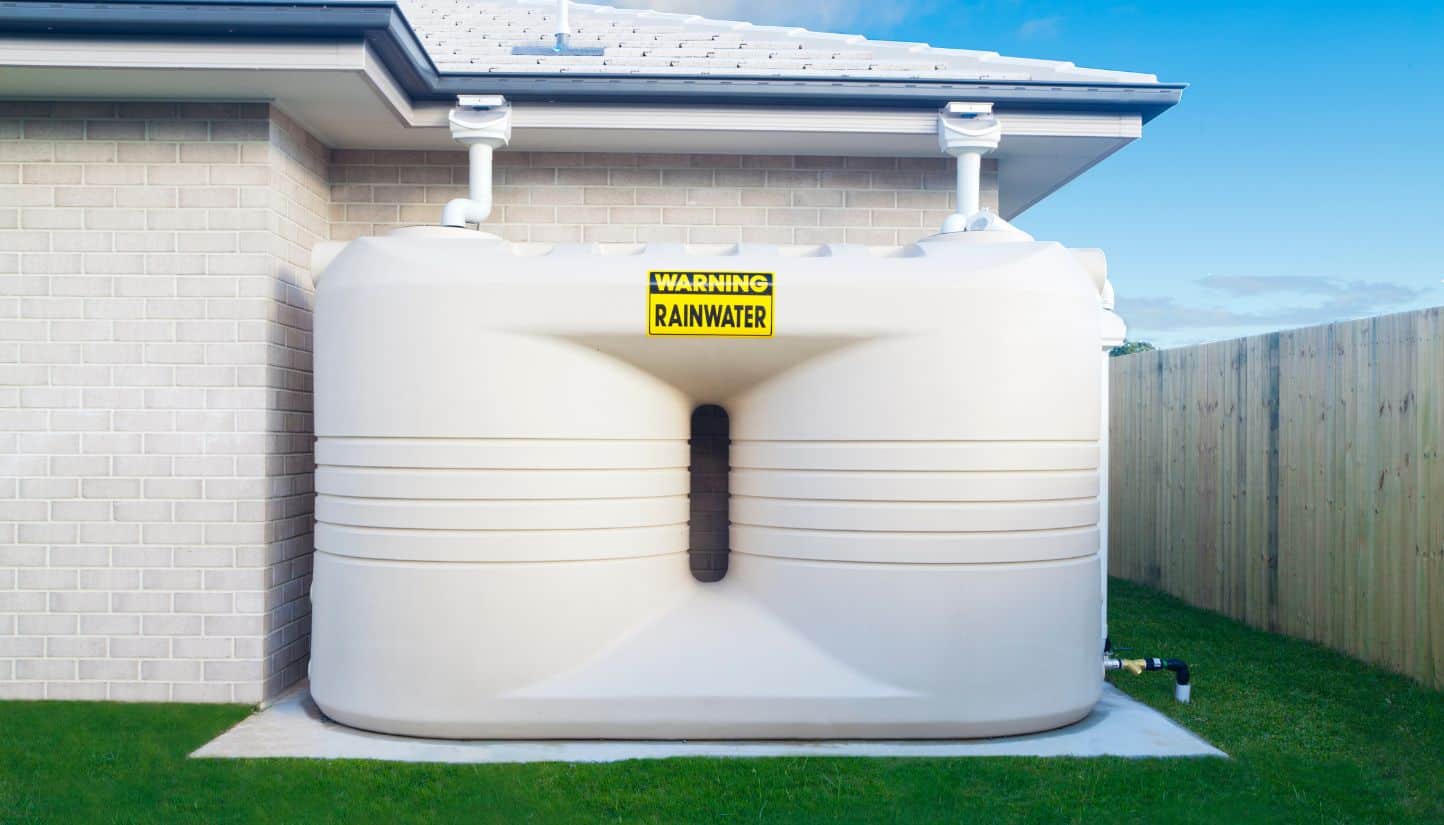 Dual rainwater tanks installed beside a house, marked with a warning sign for rainwater.