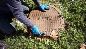 Technician opening a septic system lid in a rural area, surrounded by grass.