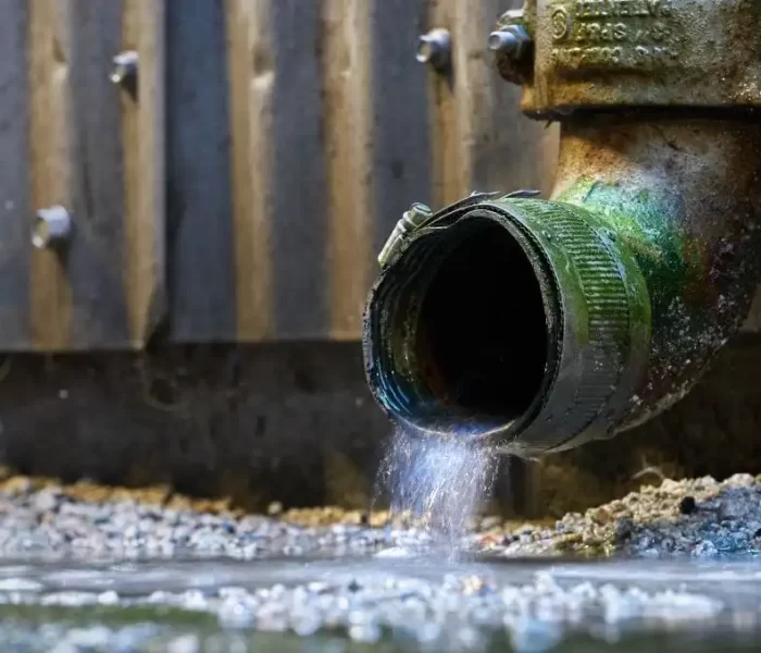 Rainwater flowing from a green metal pipe attached to a building.