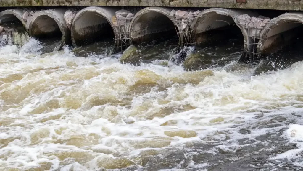 Turbulent water flowing through multiple arches in a river, showing the effects of sewerage systems.