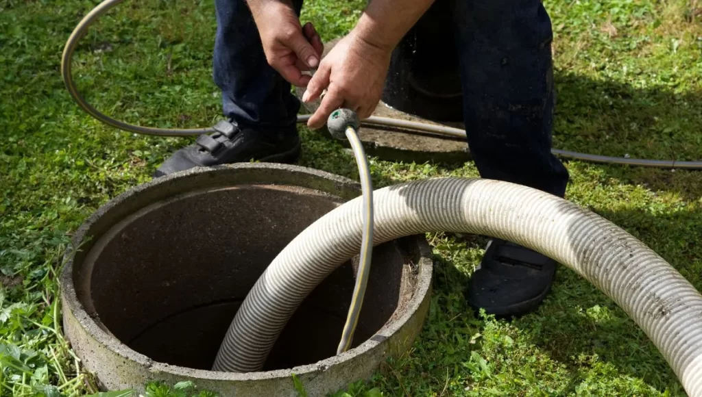 Technician servicing septic tank with suction hose in a backyard.