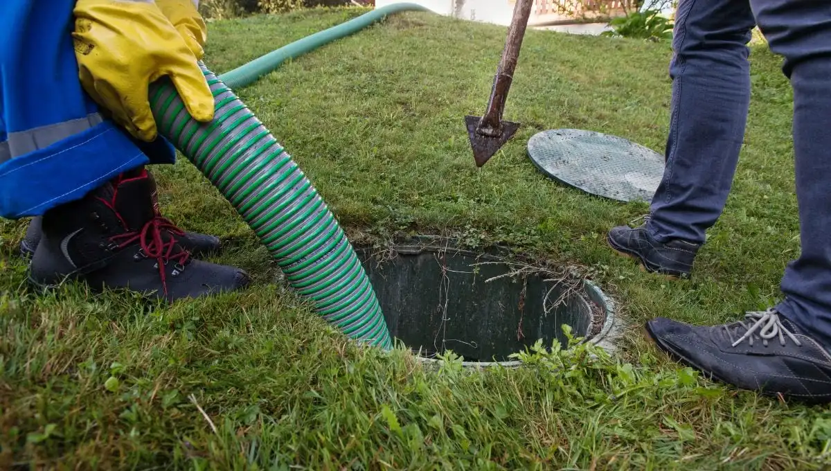 Technician using a hose to maintain a septic tank on a grassy lawn