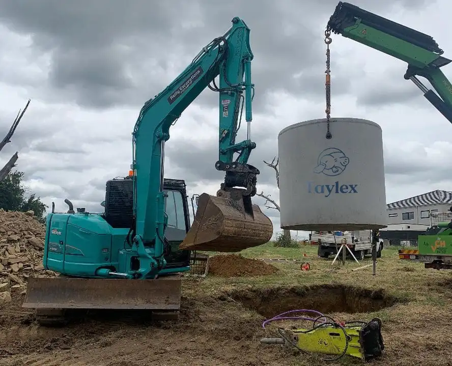 Excavator installing a Taylex septic tank at a construction site.