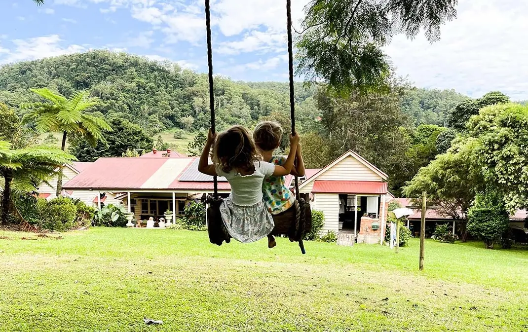 Two kids on a farm swinging on a tree, looking at their family home