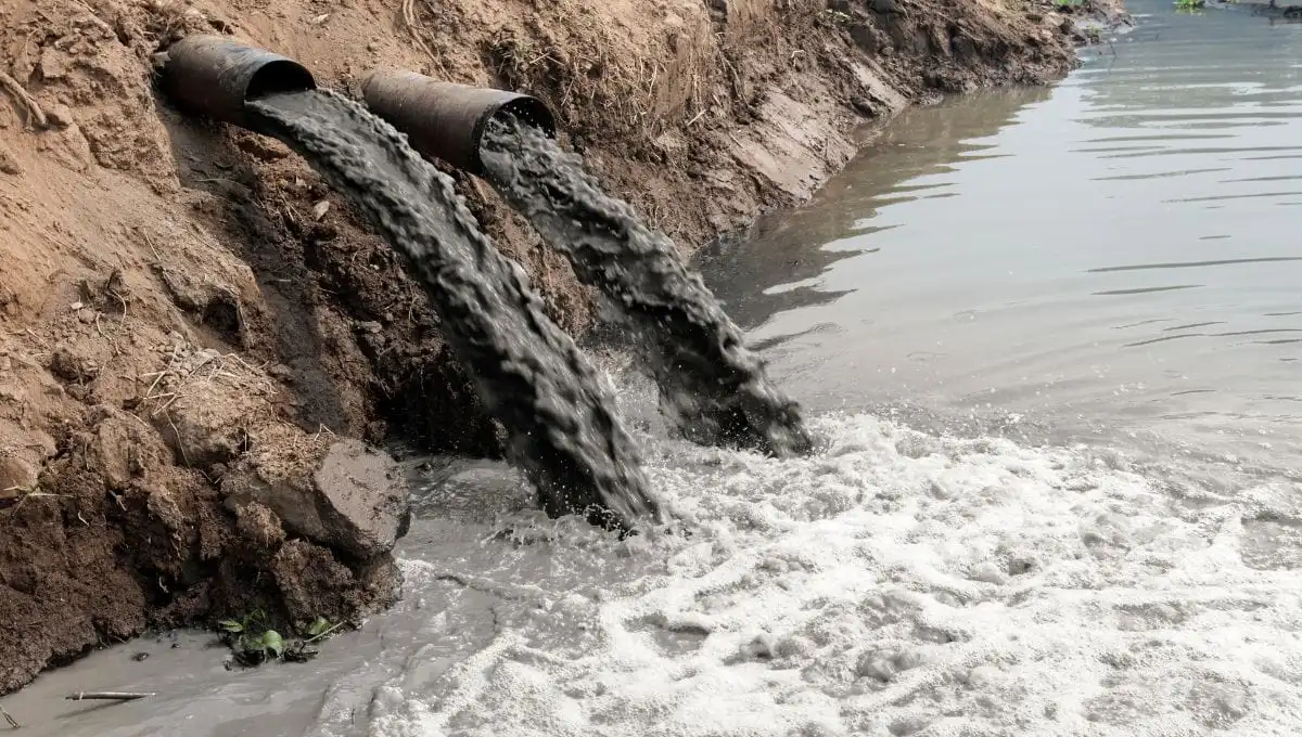Wastewater flowing into a river from two large pipes, contributing to water pollution.